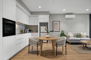 A modern kitchen with white cabinetry, a dining table with chairs, and a living area with a sofa and a coffee table. - Elevated 1-bed Apartment Near Melbourne CBD (Melbourne)