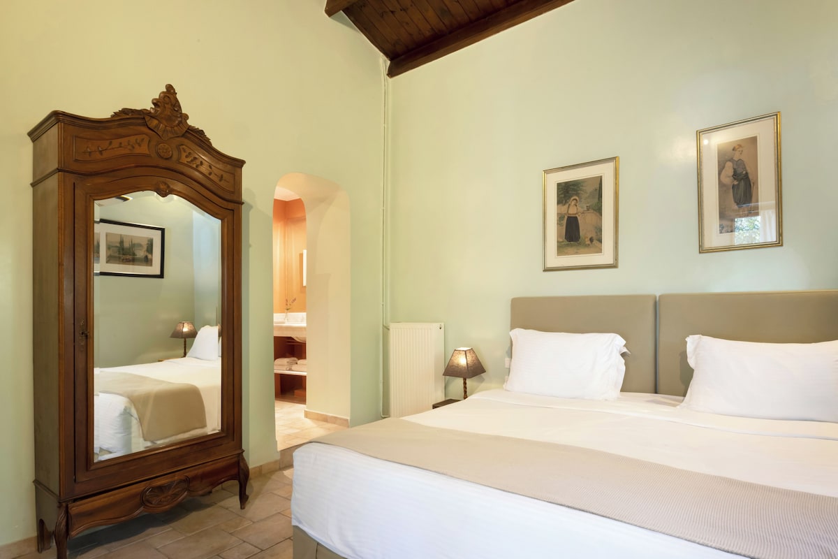 A hotel room with a large mirror, a bed with white linens, a headboard, and two framed pictures on the wall.