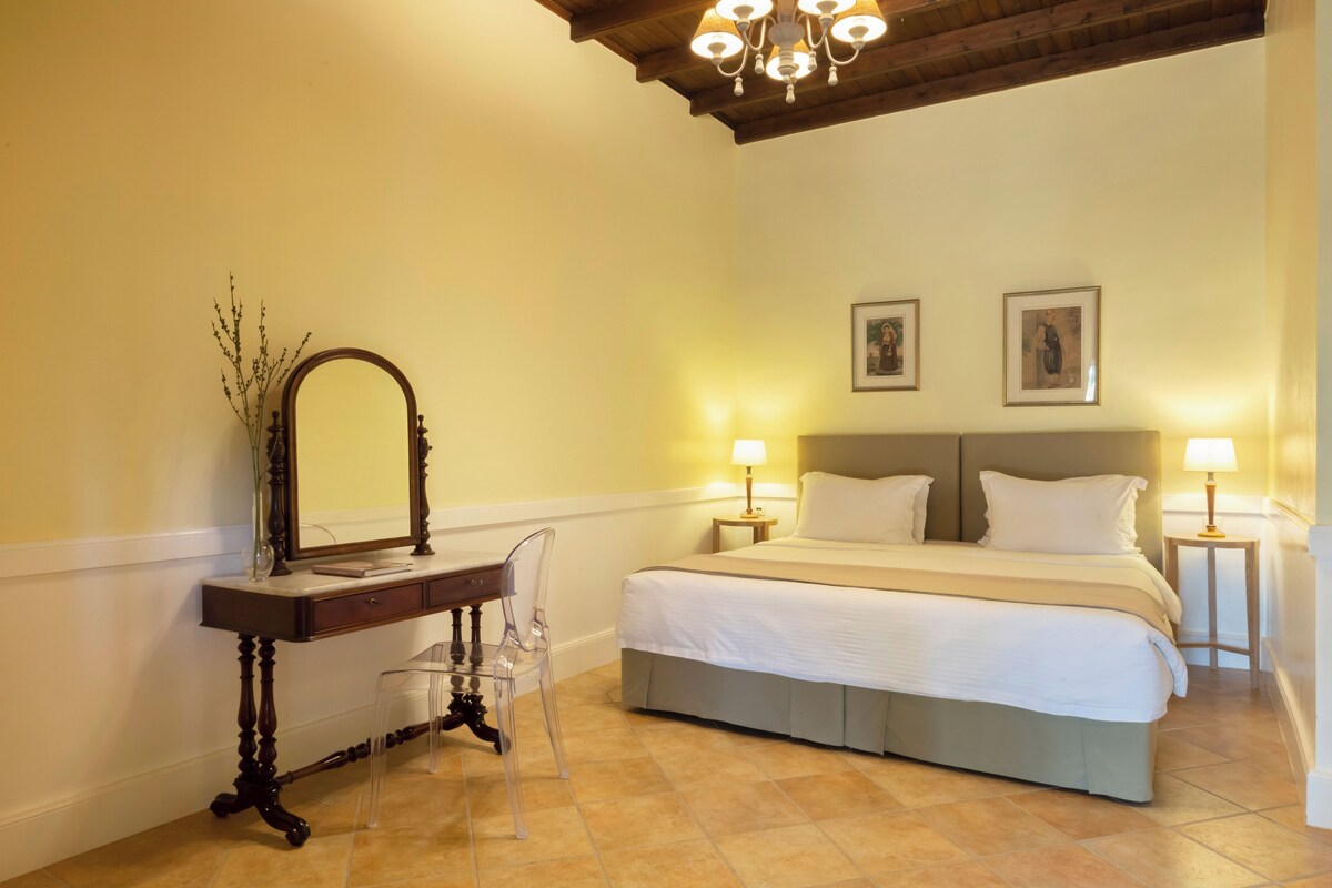 A bedroom with a bed, two bedside lamps, a nightstand, a mirror, and a vase with flowers.