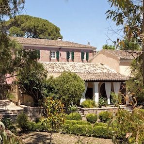 A traditional building with a tiled roof, a garden with trimmed bushes, and a tree in the background. - PELECAS COUNTRY CLUB (Corfu)