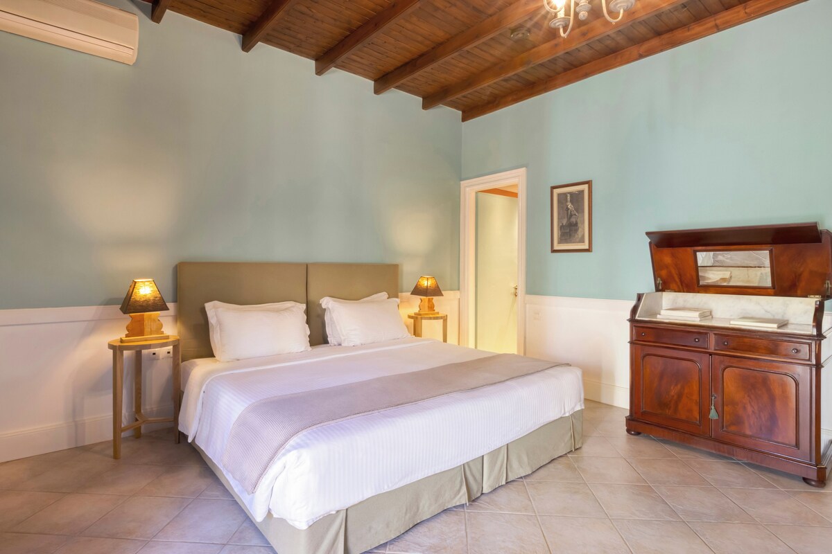 A bedroom with a bed, bedside lamps, a wooden dresser, and a door.