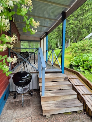 Ein überdachter Außenbereich mit Grill, Holzstufen und Blick auf einen Garten.