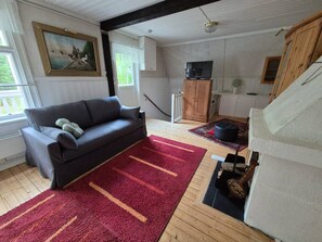 A living room with a sofa, a red rug, a wooden cabinet, and a television.