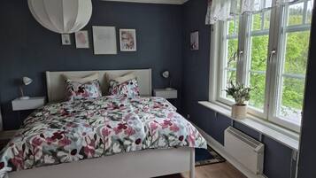 A bedroom with a bed, bedside tables, a window with curtains, and a radiator.