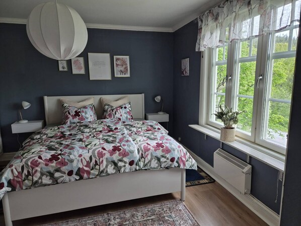A bedroom with a bed, bedside tables, a window with curtains, and a radiator.