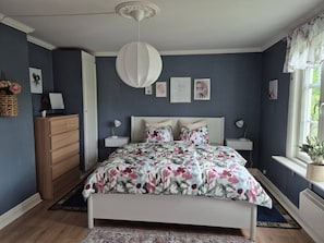 Ein Schlafzimmer mit einem Bett, Nachttischen, einer Kommode und einem Fenster mit Vorhängen.
