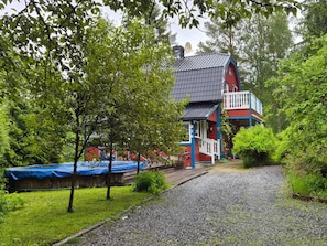 Ein zweistöckiges Haus mit roter und blauer Fassade, umgeben von üppigem Grün und einer Schotterauffahrt.