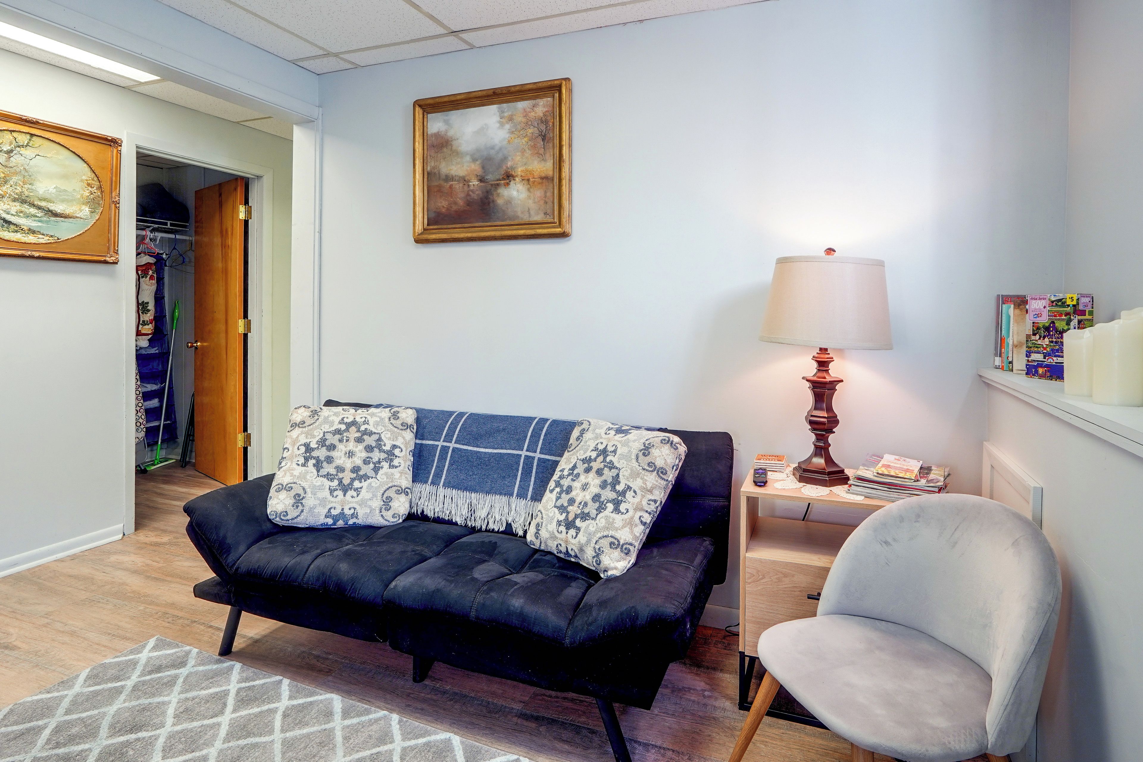 Ein Wohnzimmer mit einem schwarzen Sofa, einer blau-weißen Decke, einer Lampe und einem Sessel.