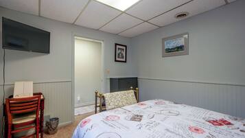 Ein Schlafzimmer mit einem Bett, einem Sessel, einem Schreibtisch, einem Fernseher und einer Tür zu einem anderen Raum.