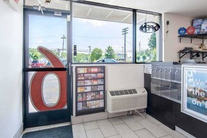 En butiksinredning med en stor, rund skylt, ett kylskåp med varor och ett fönster med utsikt över parkerade bilar och träd.