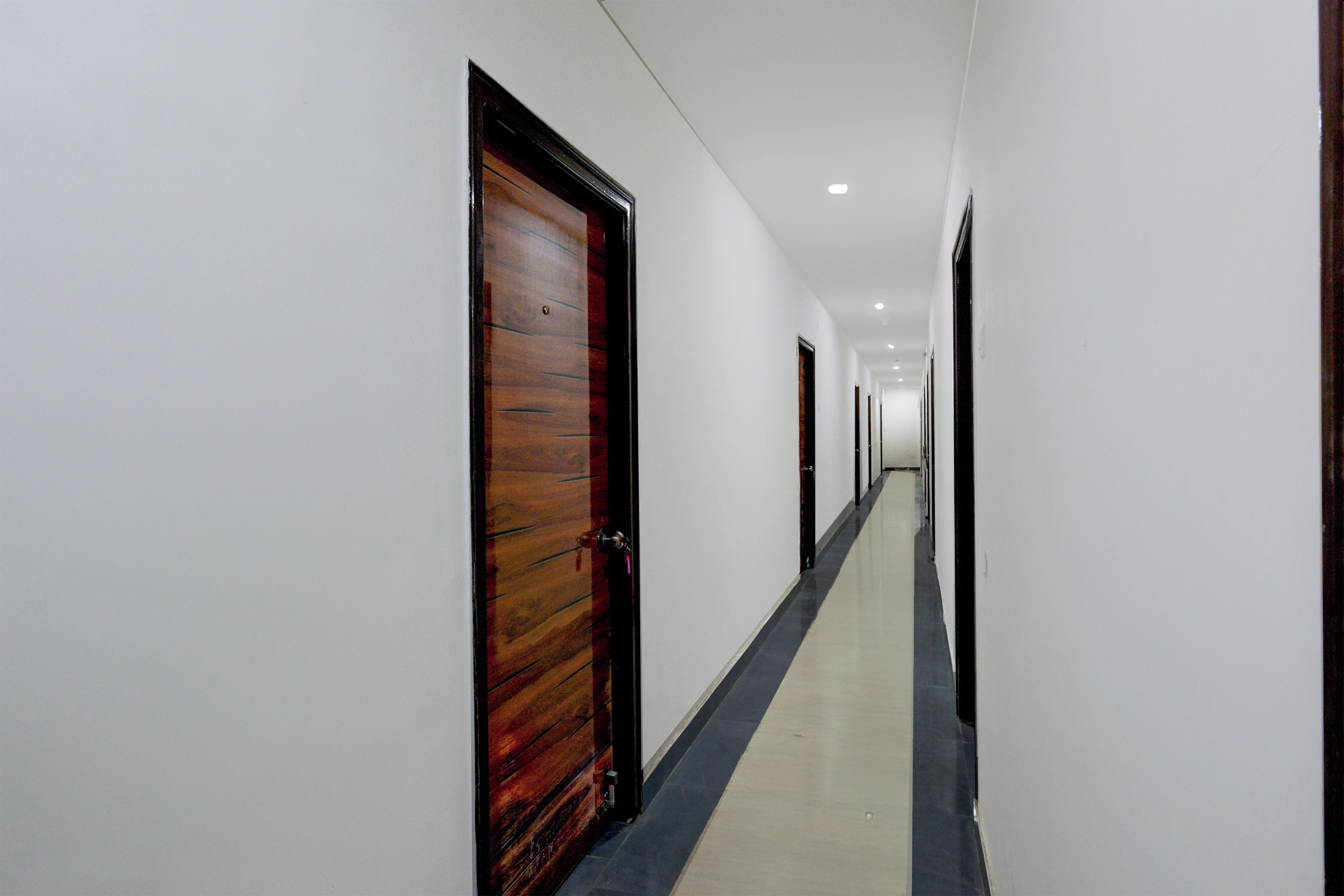 A long, narrow hallway with white walls and a wooden door on the left.