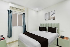 A hotel room with a bed, a bedside table, a nightstand, a window with curtains, and wall art. - Townhouse Nagole RTO Office (Hyderabad)