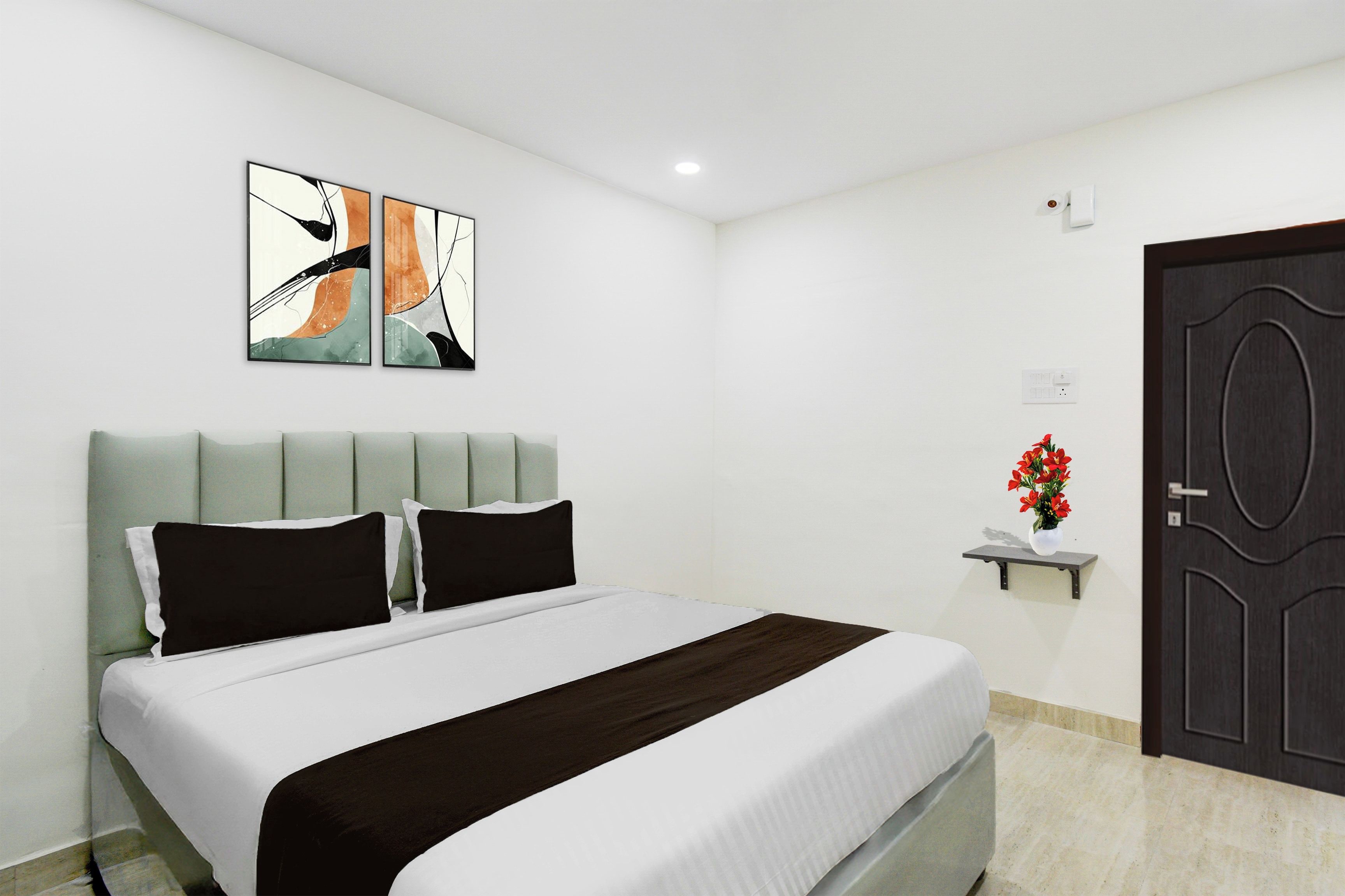 Una habitación de hotel con una cama, una obra de arte colgada en la pared, una mesita de noche con un florero y una puerta.