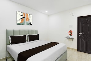 A hotel room with a bed, a wall-mounted artwork, a bedside table with a vase of flowers, and a door. - Townhouse Nagole RTO Office (Hyderabad)