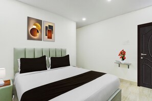 A modern bedroom with a bed, a nightstand, a wall-mounted shelf with a vase, and a door. - Townhouse Nagole RTO Office (Hyderabad)