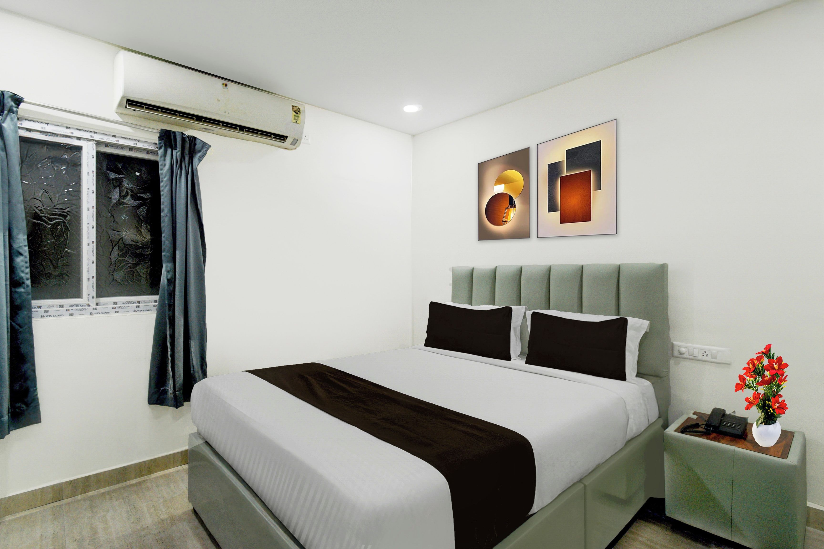 Una habitación de hotel con cama, mesita de noche, ventana con cortinas y decoración en la pared.