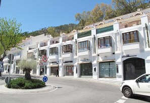 A street view with a row of white buildings, some with visible storefronts, and a white car parked on the side. - Beautiful and Elegant Penthouse in Mijas (Mijas)