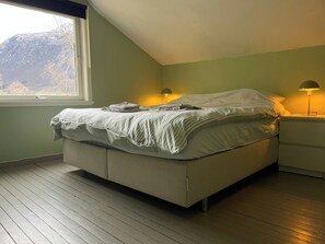 Une chambre à coucher avec un lit, une table de chevet, une lampe et une fenêtre donnant sur les montagnes.