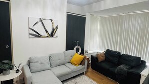 A living room with a grey sofa, a black sofa, a white side table, a floor lamp, and a painting on the wall. - Stylish 2 Bed in Manchester City Centre Fast Wi-Fi (Manchester)