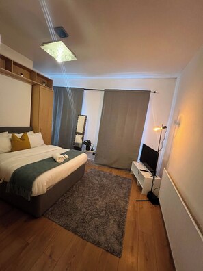 Quarto de hotel com cama, escrivaninha, televisão e uma janela grande.