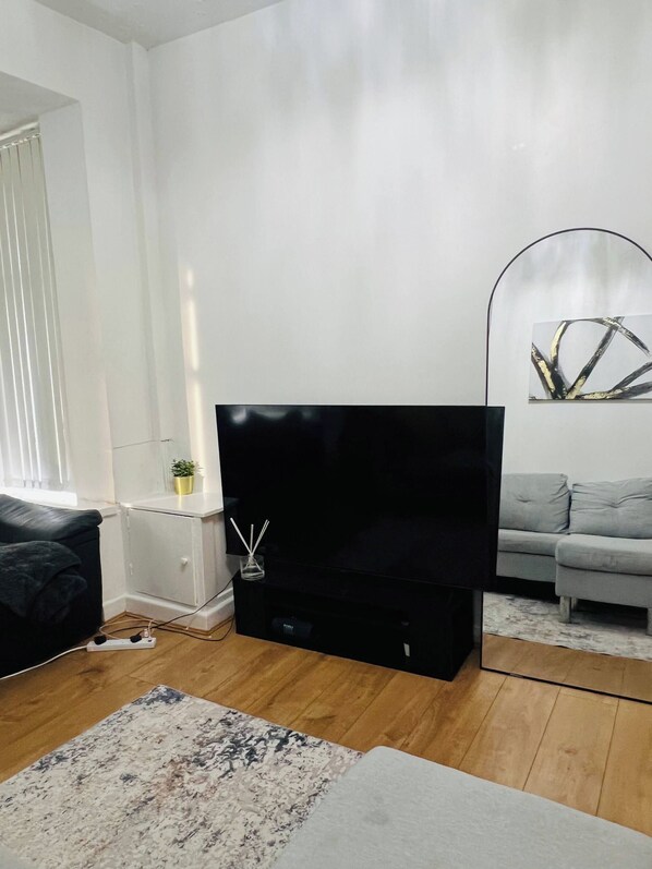 Uma sala de estar moderna com uma TV de tela plana, um sofá cinza, uma mesa de centro e um abajur.