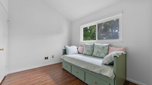 Ein Zimmer mit einem grünen Bett, weißen Wänden und einem Fenster mit Blick auf Bäume.