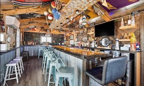 A bar area with a counter, stools, and a television screen.