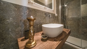 Ein Badezimmer mit Marmorwand, einem runden Waschbecken, einem Kerzenhalter und einer Duschkabine.