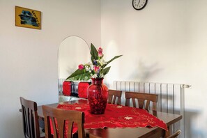 Et spisebord med et rødt dug, omgivet af træstole, en vase med blomster og et vægur.