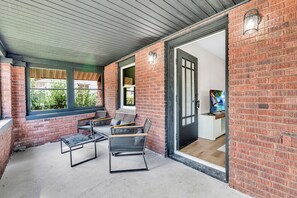 An outdoor seating area with brick walls, a covered ceiling, and a television screen. - Sunnyside Gameday House (South Bend)