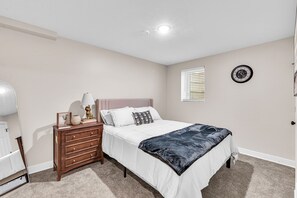 A bedroom with a bed, dresser, lamp, and wall clock. - Sunnyside Gameday House (South Bend)
