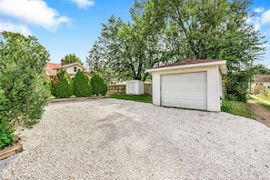 A residential driveway with a gravel surface, a garage, and a house in the background. - Sunnyside Gameday House (South Bend)