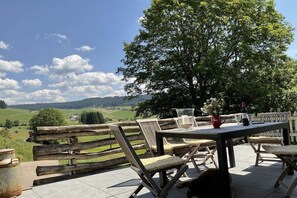 Eine Terrasse im Freien mit Tisch und Stühlen, einem Holzzaun und Blick auf eine grüne Landschaft.