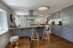 Eine moderne Küche mit grauen Schränken, einer Holzausziehtafel und zwei Barhocker.