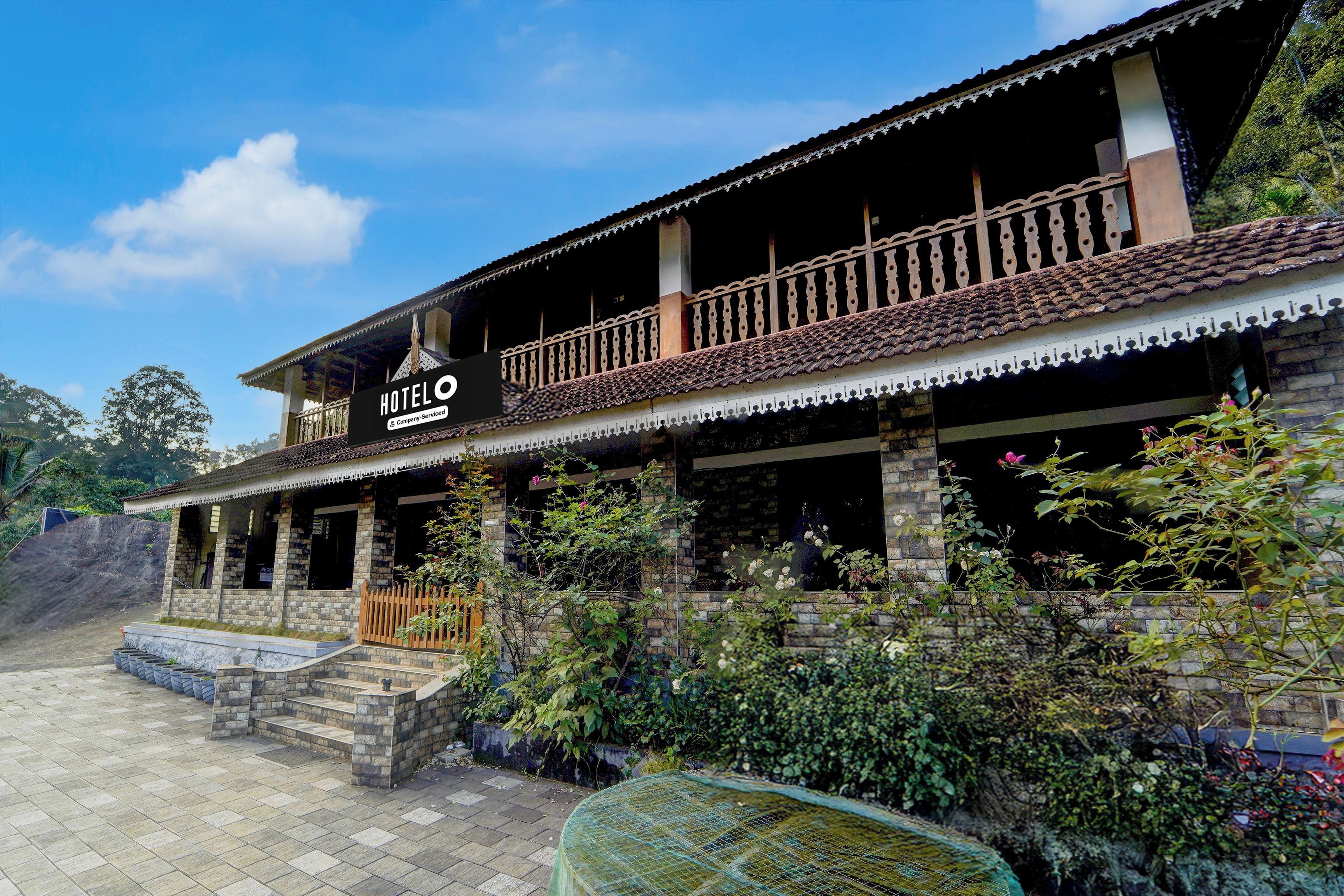 A hotel with a traditional architectural style, featuring a balcony with a decorative railing, a stone facade, and a sign indicating it is a company-serviced hotel.