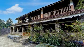 A hotel with a traditional architectural style, featuring a balcony with a decorative railing, a stone facade, and a sign indicating it is a company-serviced hotel.