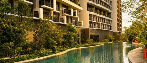 A modern high-rise building with a swimming pool and surrounding greenery.