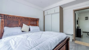 Une chambre à coucher avec une tête de lit en bois, un lit avec une literie blanche, une armoire et un miroir.