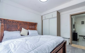 Ein Schlafzimmer mit einem hölzernen Kopfende, einem Bett mit weißer Bettwäsche, einem Kleiderschrank und einem Spiegel.