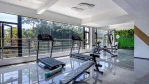 Une salle de sport moderne, dotée d’équipements d’exercice, de grandes fenêtres et offrant une vue sur la verdure.
