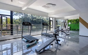 Ein modernes Fitnessstudio mit Trainingsgeräten, großen Fenstern und Blick auf Grünflächen.