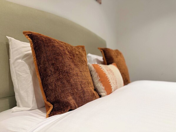 Un letto con biancheria da letto bianca e tre cuscini in diverse tonalità di marrone.