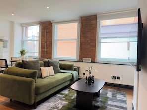 Ein Wohnzimmer mit einem grünen Sofa, einem Couchtisch und einem an der Wand montierten Fernseher.