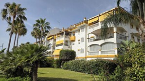 Un hotel de varios pisos con balcones, rodeado de abundante vegetación y palmeras.