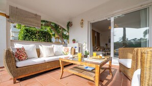 Un patio soleado con un sofá de mimbre, una mesa de centro de madera y un sillón de mimbre.