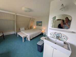 Ein Schlafzimmer mit Bett, Nachttisch, Bank, Kommode, Spiegel und einem kleinen Mülleimer.