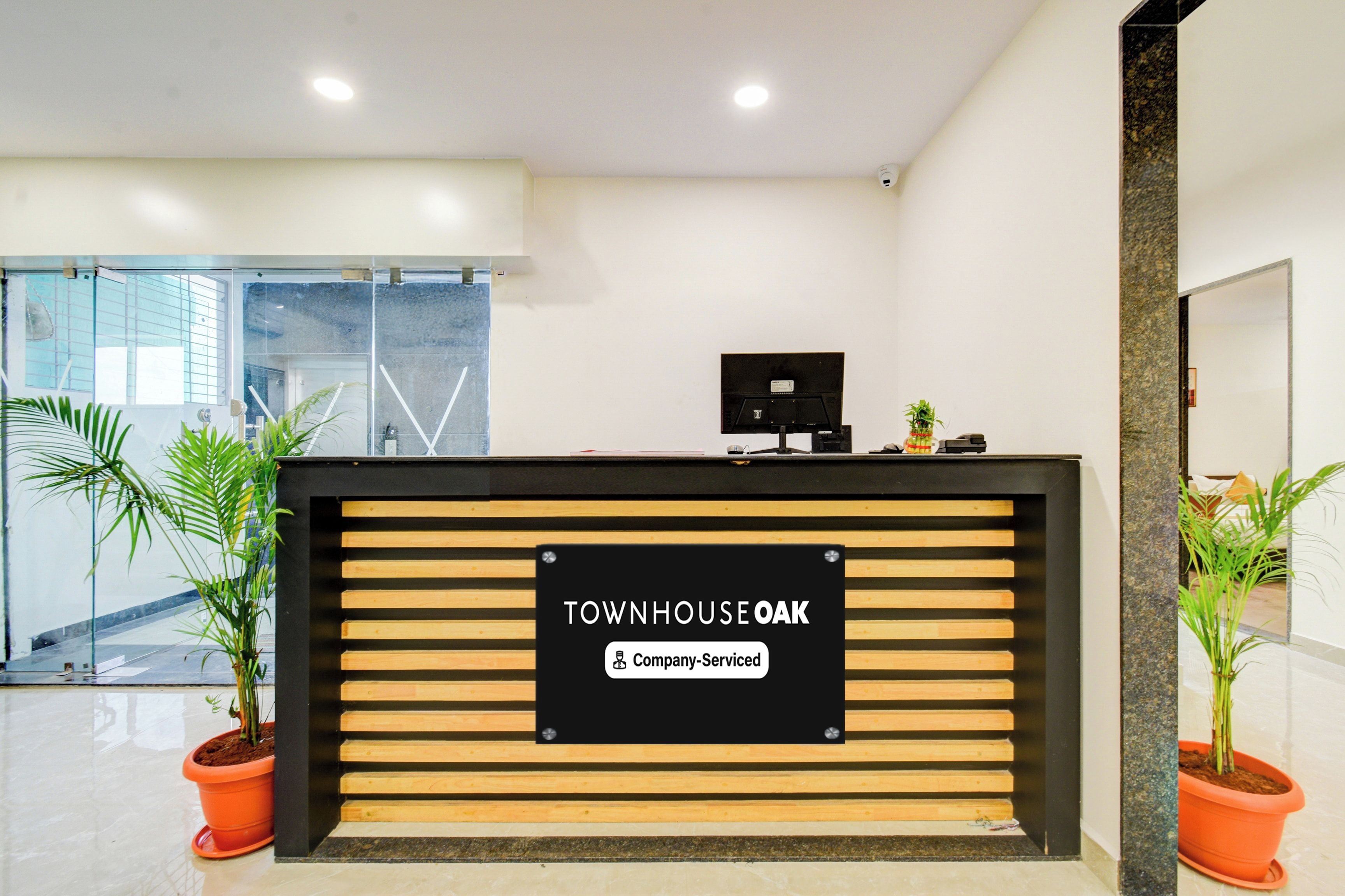 Un mostrador de recepción con un cartel que indica 'Company Serviced' y una zona de espera con plantas en macetas y un muro de cristal.