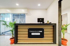 A reception desk with a sign indicating 'Company Serviced' and a reception area with potted plants and a glass wall.