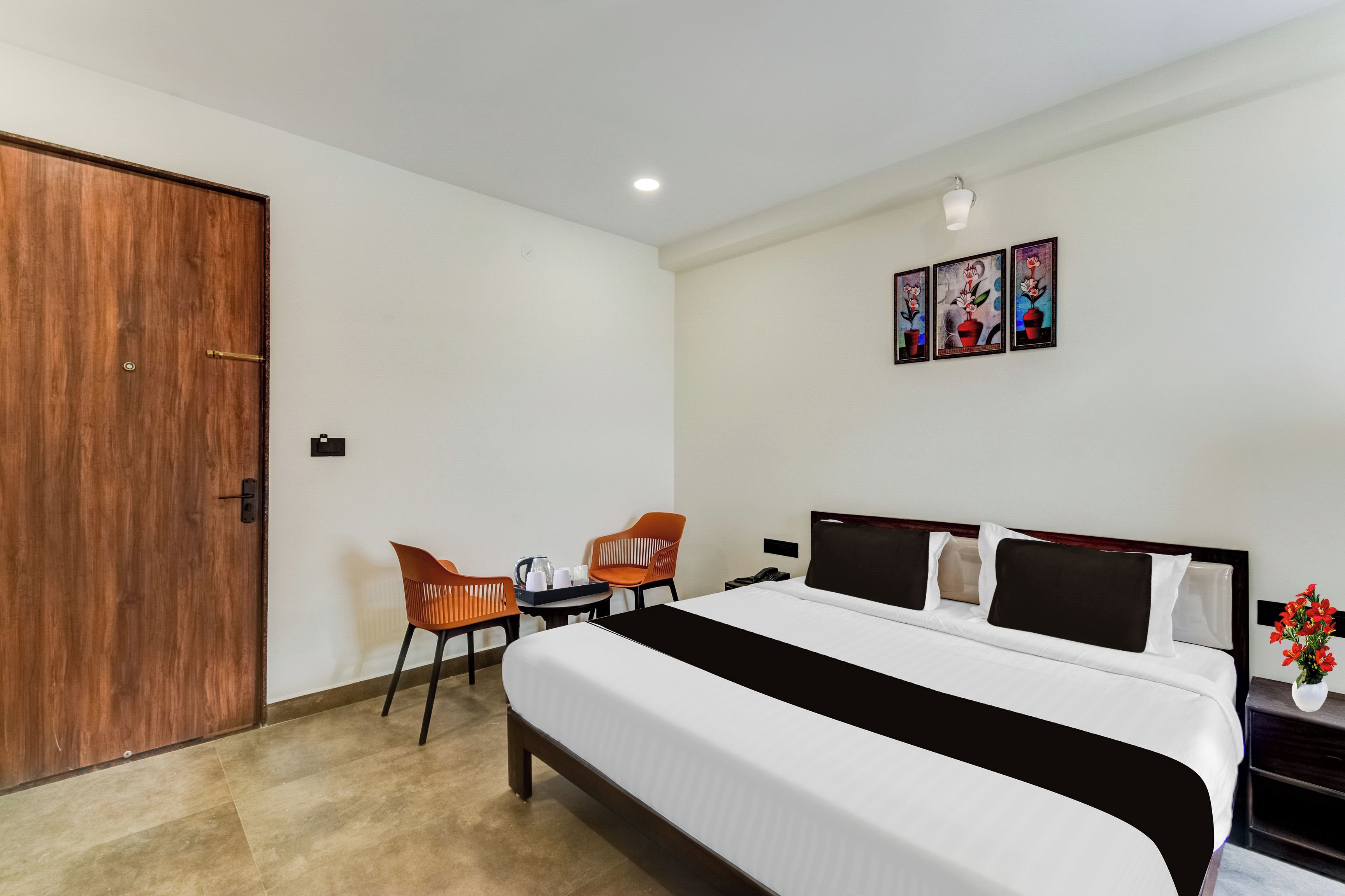 Habitación de hotel con una cama grande, dos sillas, una mesita con bandeja, una mesita de noche, un teléfono y una obra de arte colgada en la pared.