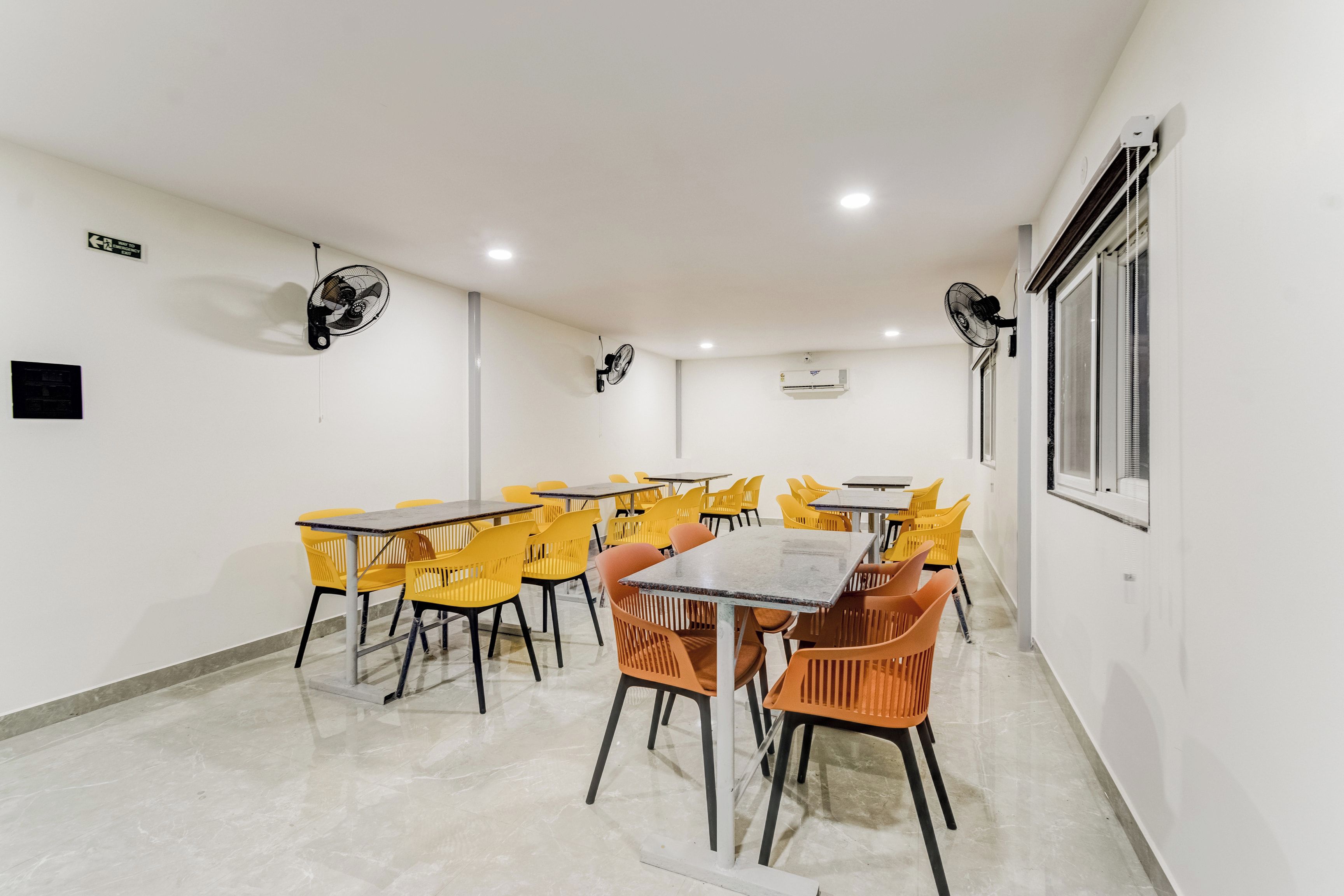 Una sala de conferencias con varias mesas y sillas, ventiladores de techo, un letrero de salida de emergencia y un equipo de aire acondicionado.